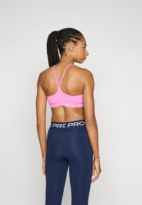 Pink sports bra with a wide white band featuring "NIKE," paired with navy high-waisted leggings, showing a smooth, fitted design.