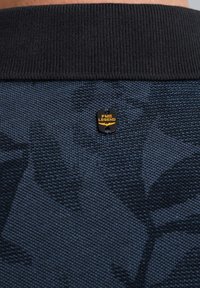 Tissu texturé bleu marine avec un motif de feuilles subtil et un col noir côtelé. Un logo PME Legend noir et jaune est fixé à l'arrière.
