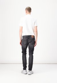 Jean slim noir avec une texture délavée, poches arrière et détails de couture visibles. Associé à un t-shirt blanc uni à manches courtes et des baskets.