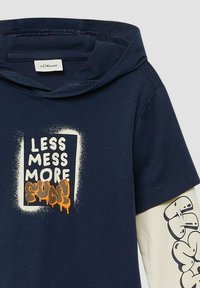 Granatowa koszulka z kapturem w kształcie kangura, z białym i pomarańczowym tekstem w stylu graffiti "Mniej bałaganu, więcej zabawy!" oraz wzorzystymi kremowymi rękawami.