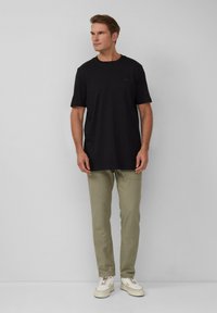 Zwarte katoenen t-shirt met korte mouwen gecombineerd met lichtgroene slim-fit broek en witte sneakers, gepresenteerd tegen een neutrale achtergrond.