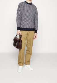 Laivastonsininen kuvioitu neulepusero, beiget housut, valkoiset tennarit ja ruskea nahkainen olkalaukku hopeisilla soljilla, kädessä pidettävä.