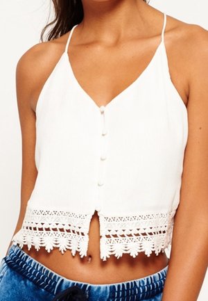 Top corto blanco sin mangas con tirantes finos, botones al frente y borde de encaje en el dobladillo, combinado con pantalones azules con cordón.