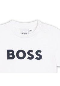Hvit bomulls-T-skjorte med stor mørkeblå "BOSS"-logo på forsiden. Inkluderer to trykknapper på skulderen for enkel påkledning.