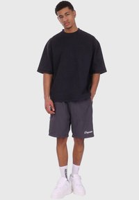 Sort oversized t-shirt, korte grå shorts med hvid "Dgsize" logo, hvide sneakers og strukturerede hvide sokker. Enkel og afslappet outfit.