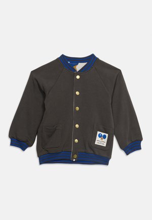 Veste varsity enfant gris foncé avec col, poignets et ourlet rayés bleus, boutons dorés, deux poches devant et écusson avec des ballons bleus sur la poche.