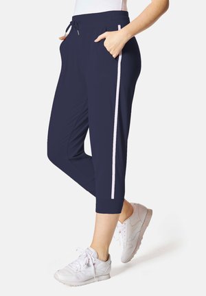 Marineblaue Cropped-Hosen mit weißem Streifen an der Seite, Kordelzugbund, Taschen, getragen mit weißen Sneakers.