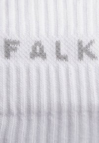 Biały, prążkowany materiał z napisem "FALK" w jasnoszarym, lekko wypukłym kroju pisma. Gładka tekstura z naprzemiennymi prążkami.