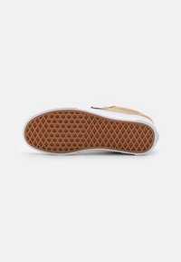 Talpa de tenişi în stil Vans, cu un model de profil în fagure din cauciuc maroniu, încadrată de o bandă de cauciuc alb.