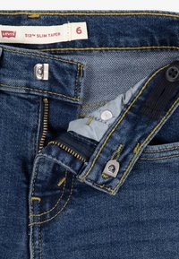 Siniset Levi's 512 Slim Taper -farkut koossa 6, jossa osittain avattu vetoketju ja näkyvissä oleva nappi sekä metallinen koukkukiinnitys.