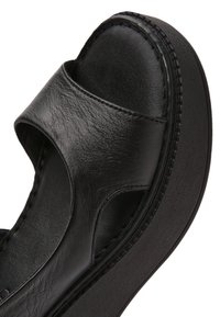 Sandale plateforme en cuir noir avec bout ouvert et large sangle à l'avant, dotée d'une semelle épaisse texturée et de coutures apparentes.