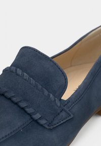 Ναυτικά loafers από σουέτ με ραμμένο λουράκι, στρογγυλεμένη μύτη και χαμηλό ταμπά τακούνι. Ομαλή υφή και μινιμαλιστικός σχεδιασμός.