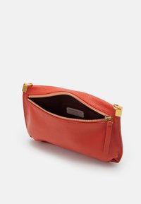 Clutch de cuero rojo con acabado texturizado, herrajes en tono dorado y cremallera en la parte superior. El interior presenta un forro oscuro y una etiqueta de la marca.