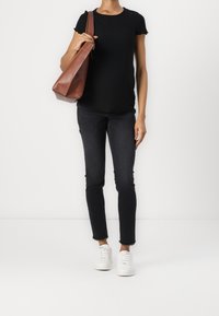 Black ribbed short-sleeve top, paired with dark skinny jeans and white sneakers. A brown leather shoulder bag is held in the left hand.