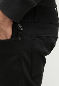 Svart denimjeans med slim fit. Har en framficka med knapp och synlig sömnad. Märke "Replay" på midjebandet.