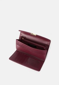 Burgundy tekstiilitodistamaton nahkalompakko kultaisella soljella, jossa on useita korttipaikkoja, vetoketjullinen tasku ja läpinäkyvä henkilökorttinäkymä. Sujuva pinta.