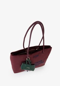 Borsa a spalla color mogano con doppio manico marrone, chiusura con zip e portachiavi in pelle verde. Presenta dettagli testuali blu su un lato. Texture liscia.
