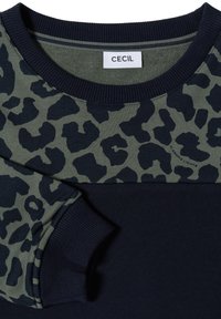 Partie haute à imprimé léopard vert et noir avec col rond côtelé bleu marine et poignets de manches, étiquette "CECIL" à l’intérieur du col.