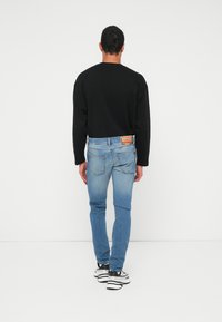 Musta pitkähihainen paita, vaaleansiniset kapeat farkut haalistuneella tekstuurilla ja mustavalkoiset lenkkarit. Huomionarvoinen takataskun merkki.