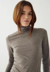 Pelēks ar garām piedurknēm tērpis ar augstu apkakli, izgatavots no mīkstas, teksturētas auduma. Pieguļošs dizains ar gludu apdari un smalkiem šuvju akcentiem.