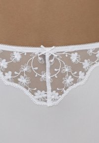 Witte kanten onderkleding met bloemendessin op de tailleband, voorzien van een satijnen strikdetail in het midden en een gladde stof.