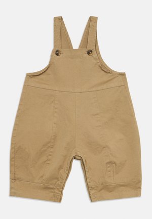 Beige kurze Latzhose für Kleinkinder mit Schultergurten, Knopfverschlüssen an der Brust und Druckknöpfen an den Innenbeinnähten für einfaches Windelwechseln.
