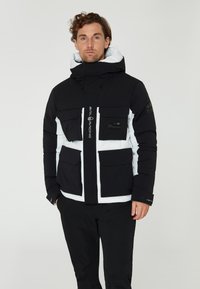 Svart och vit pufferjacka med huva, som har fyra framfickor, dragkedja och logotypdetaljer. Tillverkad av isolerat material.