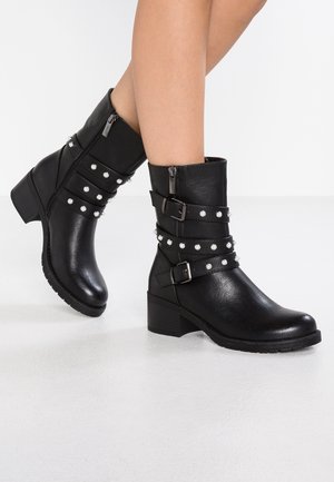 Bottines noires en matériau synthétique texturé, dotées de trois sangles avec boucles ornées de clous en argent et d'un petit talon carré.