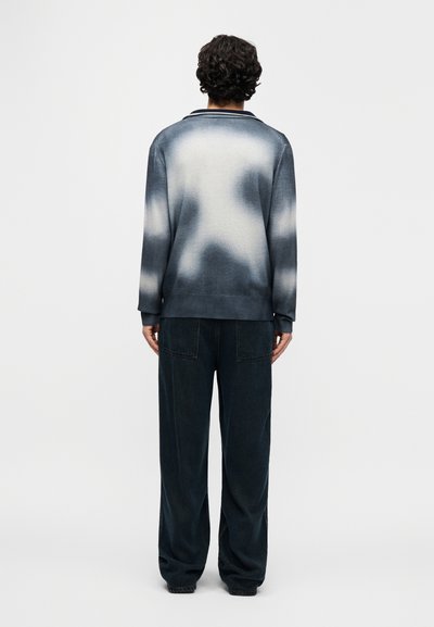 Πλεκτό πουλόβερ σε διαβαθμισμένες αποχρώσεις μπλε και γκρι με απαλή υφή, συνδυασμένο με χαλαρό, σκούρο τζην παντελόνι με τσέπες πατς.