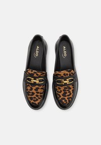 Mocassins en cuir noir avec un panneau en tissu au motif léopard et des détails en métal doré. Texture lisse et design classique à enfiler.