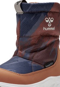 Vattentålig ankelboot med blå och röda mönstrade textilöverdelar, nedre del i brun läder och vit gummisula. Har logotyp och dragtab.