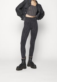 Kvinna klädd i en svart cropped jacka, grårandig tubtopp, svarta och grå randiga leggings samt svarta plattformsskor med snörning.