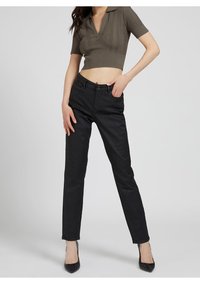 Pantalons sombres coupés en tissu lisse, avec une coupe classique et des poches avant. Associés à un polo ajusté de couleur vert olive.