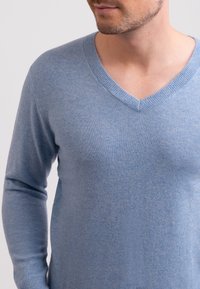 Vaaleansininen V-pääntie neulepaita, joka on valmistettu pehmeästä, teksturoidusta kankaasta ja jossa on pitkät hihat. Tiivis malli korostaa kaula-aukkoa ja vartalon muotoa.