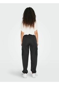 Zwarte cargobroek met elastische tailleband, zijzakken en omgeslagen zoom, gecombineerd met een witte oversized top. Model is van achteren afgebeeld.