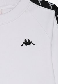 Felpa bianca con ricamo del logo Kappa nero sul davanti. Accenti neri con motivo sulle cuciture delle spalle. Morbido materiale in cotone.