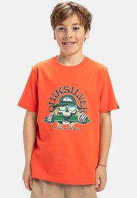 Oranžové bavlněné tričko s grafikou kostry se slunečními brýlemi a zeleným předmětem, s textem "Quiksilver" nad designem.