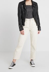 Schwarze Leder-Bikerjacke, graues Strickoberteil, cremefarbene, cropped Jeans mit ausgefranstem Saum und schwarze Sneakers mit weißen Schnürsenkeln und Punkten.