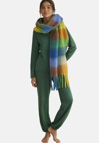 Ensemble de salon vert comprenant un haut à manches longues et un pantalon fuselé, associé à une écharpe à franges multicolore avec des rayures vives de bleu, jaune et vert.