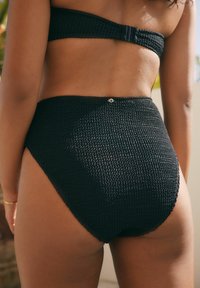 Czarny dół bikini wykonany z teksturowanej tkaniny o wysokim stanie. Posiada mały złoty akcent z tyłu.