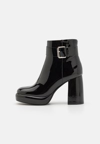 Botines de charol negro con un amplio tacón cuadrado, punta redondeada y una correa ajustable con hebilla alrededor del tobillo.