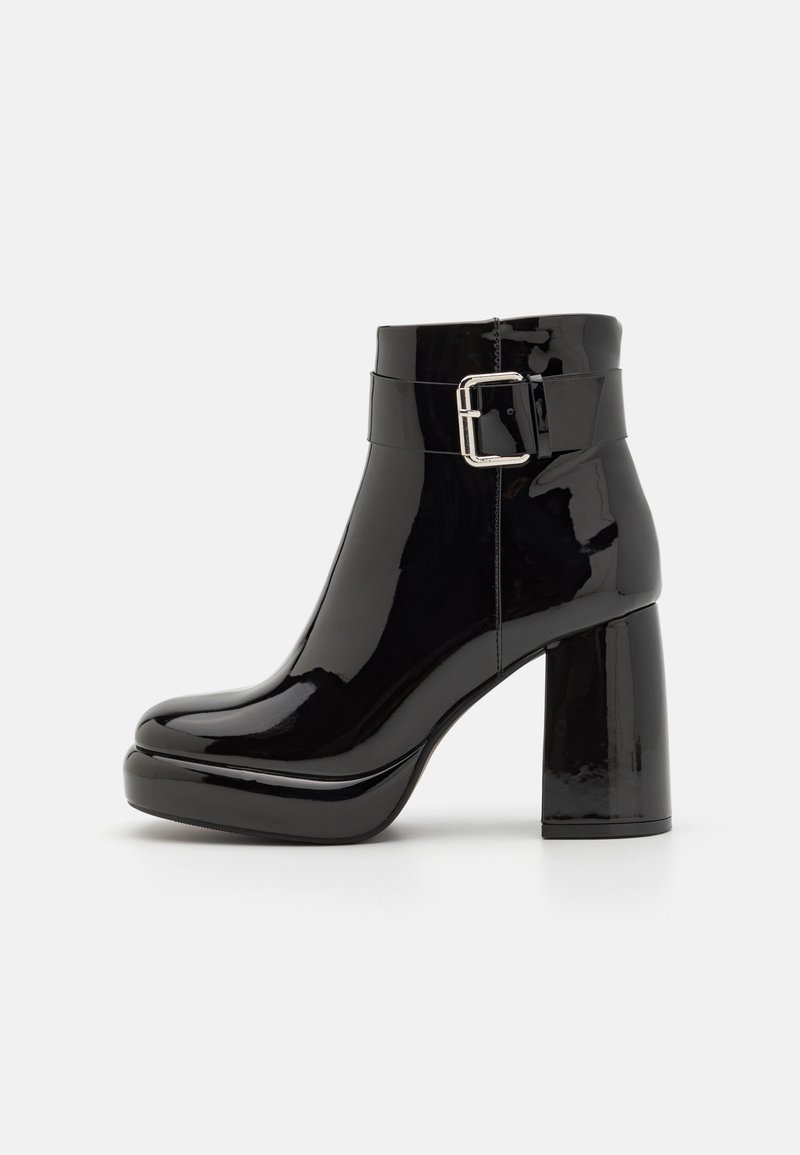 Botines de charol negro con un amplio tacón cuadrado, punta redondeada y una correa ajustable con hebilla alrededor del tobillo.