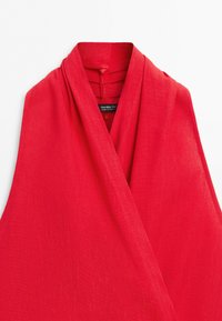Red sleeveless wrap style top with a deep V-neck and padded shoulders, made from textured fabric.