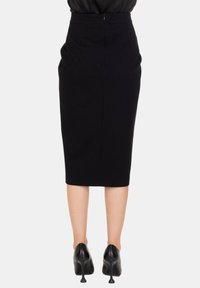 Gonna a matita nera con design fino al ginocchio, texture liscia e cerniera posteriore, abbinata a scarpe nere con tacco alto.