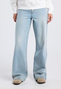 Light blue, flared jeans made of denim with a faded finish. Features subtle stitching details and wide leg openings, worn with beige footwear.