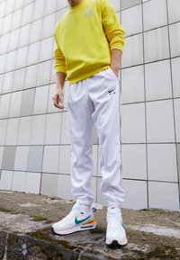 Žlutá mikina s logem Nike, bílé kalhoty s černými detaily a bílé tenisky s tyrkysovými a oranžovými prvky.