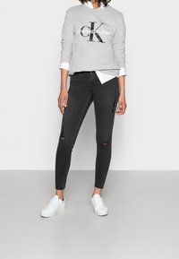 Sweat-shirt gris avec le logo « CALVIN KLEIN JEANS », associé à un jean skinny noir avec des déchirures aux genoux et des sneakers blanches.