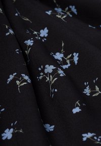 Tissu noir avec un motif floral comportant des fleurs bleu clair et des tiges vertes, affichant une texture douce et une apparence drapée.