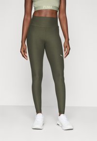 Vihreät korkeavyötäröiset legginsit, joissa on sileä kangas ja tiukka muotoilu, ja joissa on kultainen Puma-logo nilkan lähellä. Yhdistetty valkoisiin tennareihin.