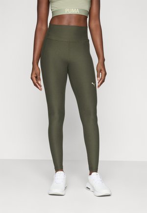Green high-waisted leggings with a smooth texture and fitted design, featuring a gold Puma logo near the ankle. Worn with white sneakers.
